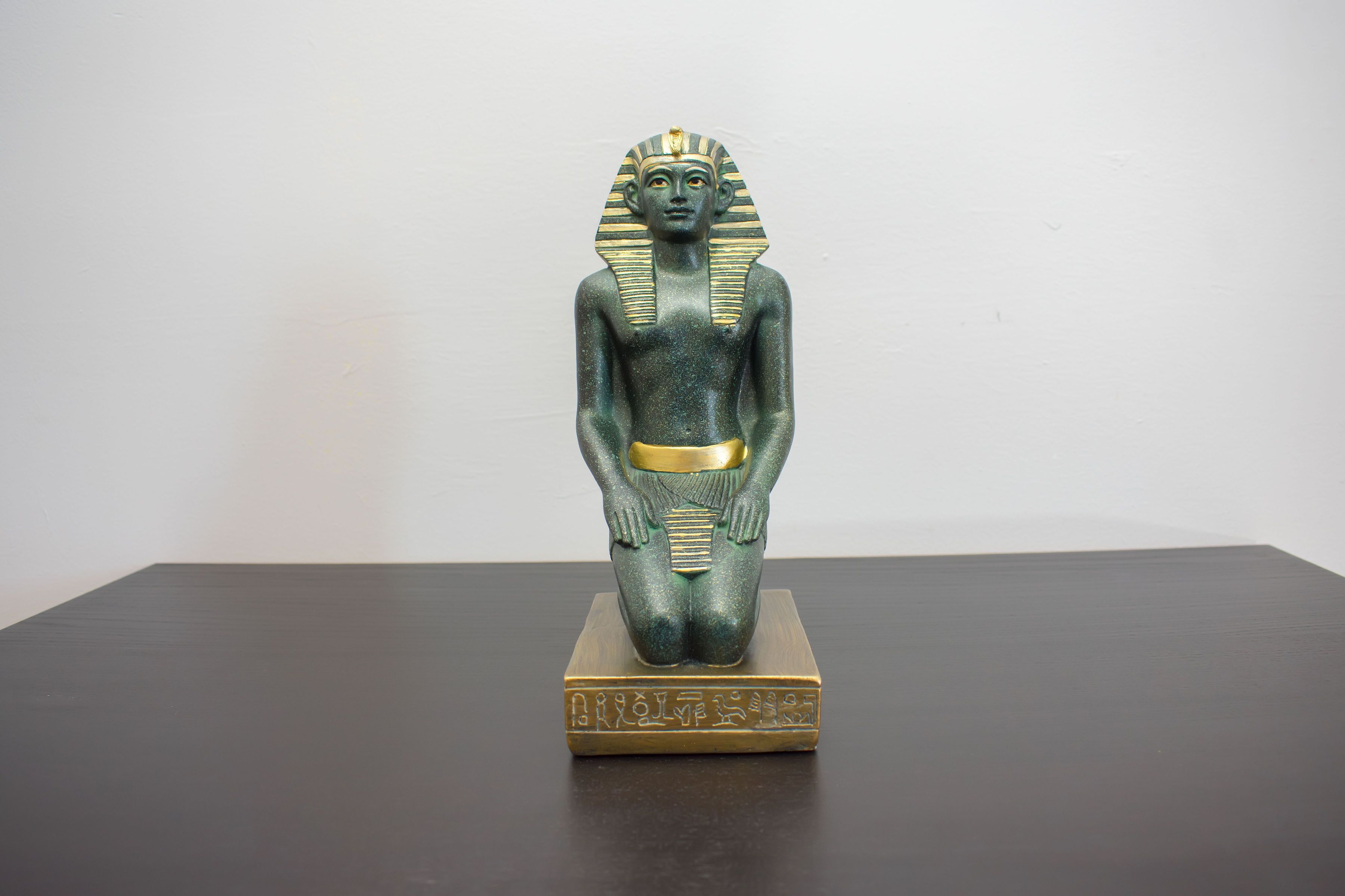 Una estatua de una figura con tocado, sobre un pedestal con inscripciones.