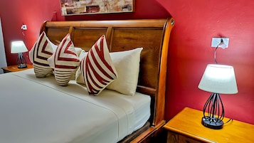 Una cama bien tendida con almohadones a rayas, un cabecero de madera y lámparas de noche sobre mesitas de madera.