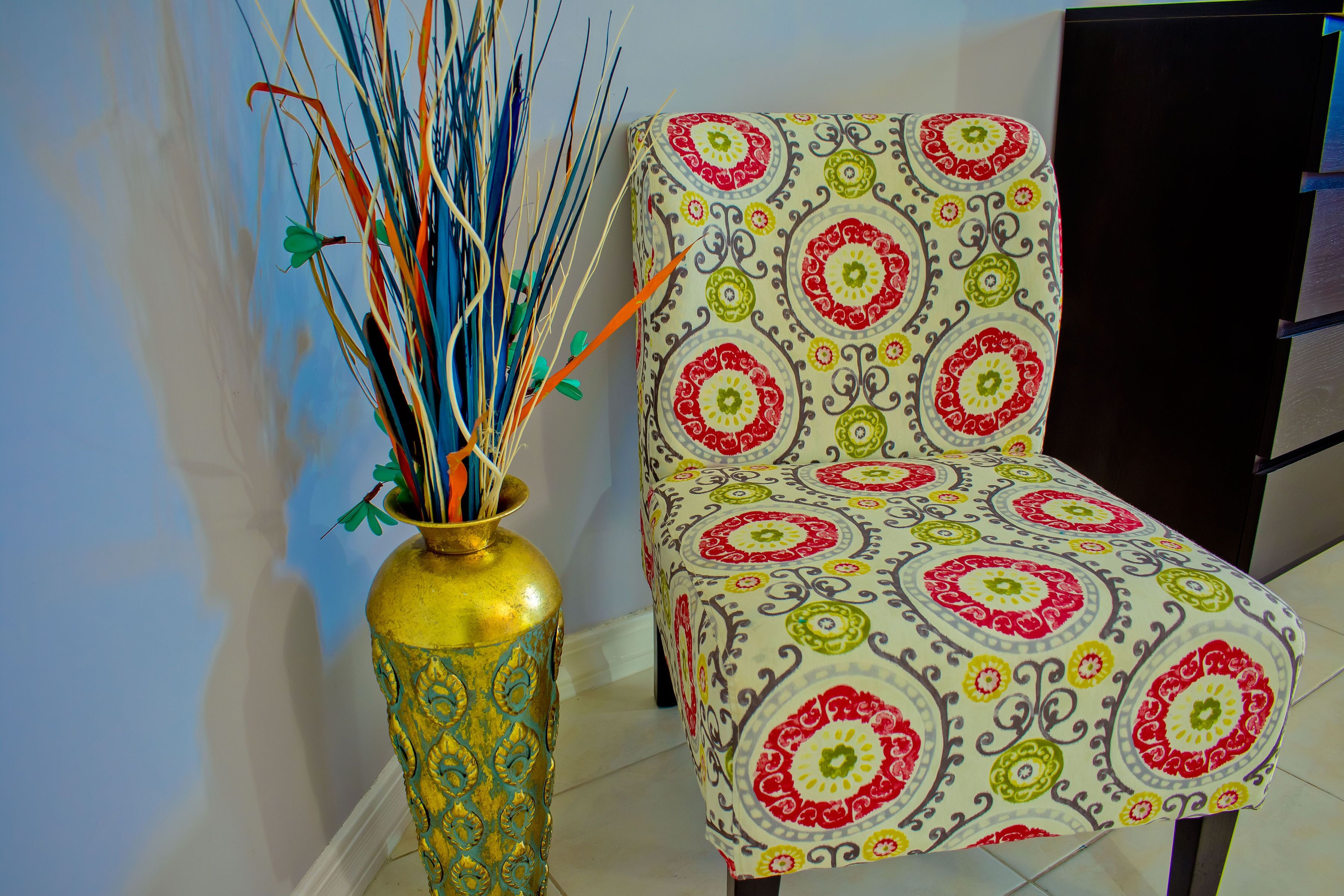 A chair with a patterned fabric and a decorative vase with sticks.