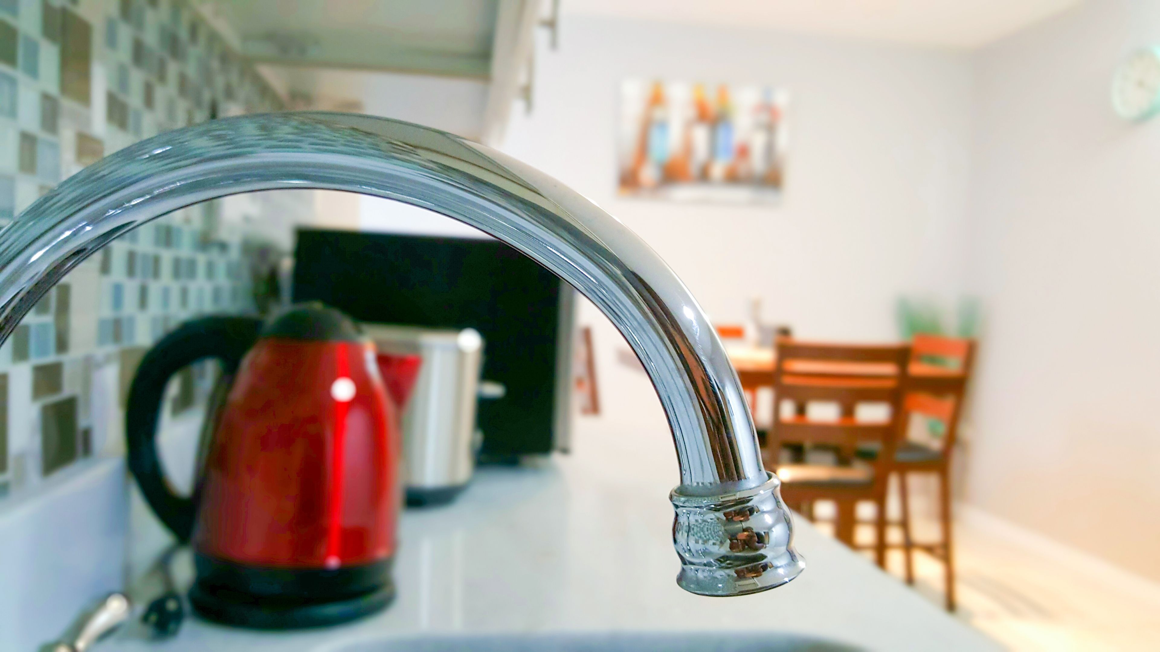 A kitchen with a modern faucet, a red kettle, and a dining area with a wooden table and chairs.