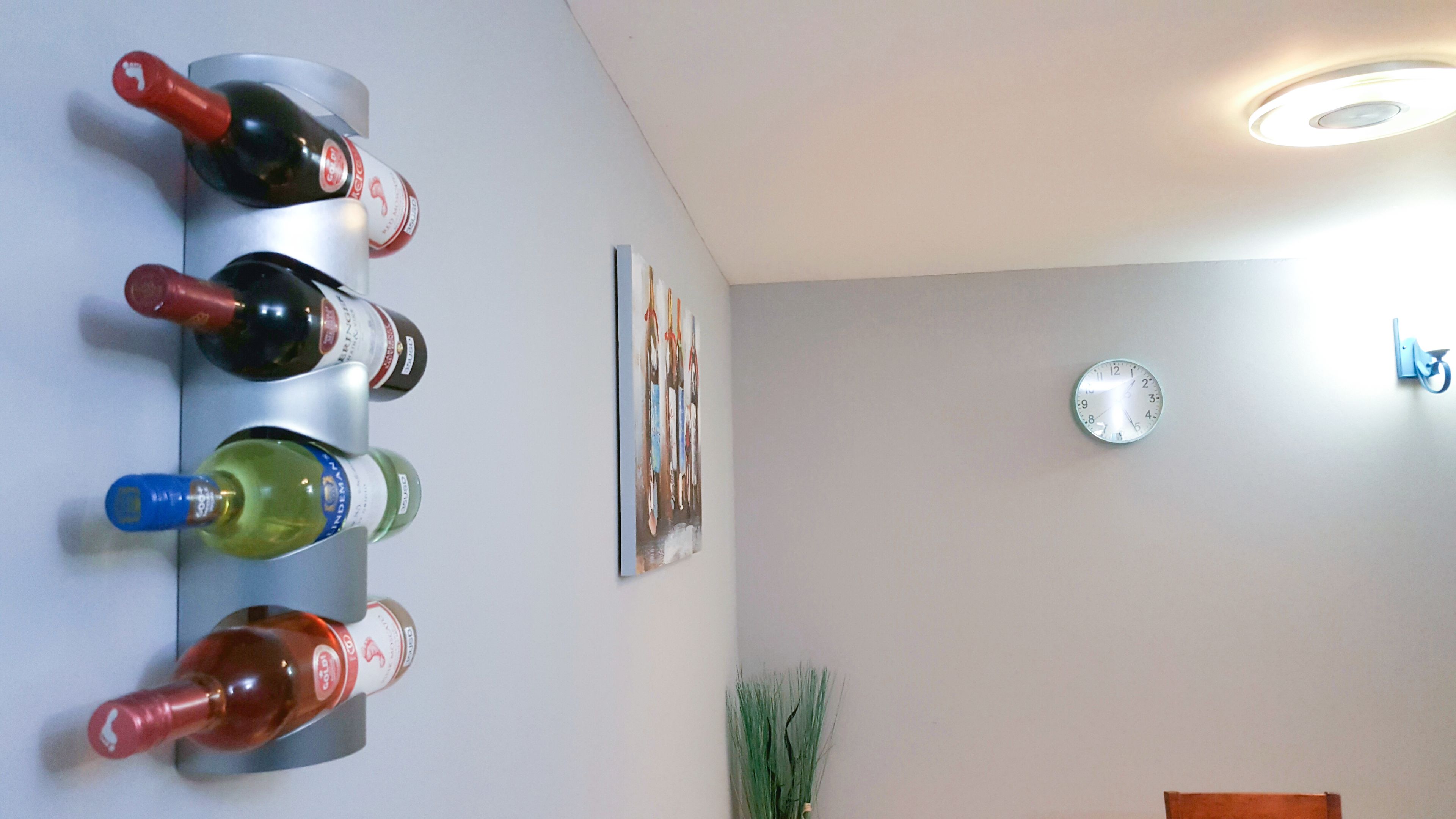 Ein an der Wand befestigter Weinkühler mit Flaschen, einer Uhr und einer kleinen Pflanze.