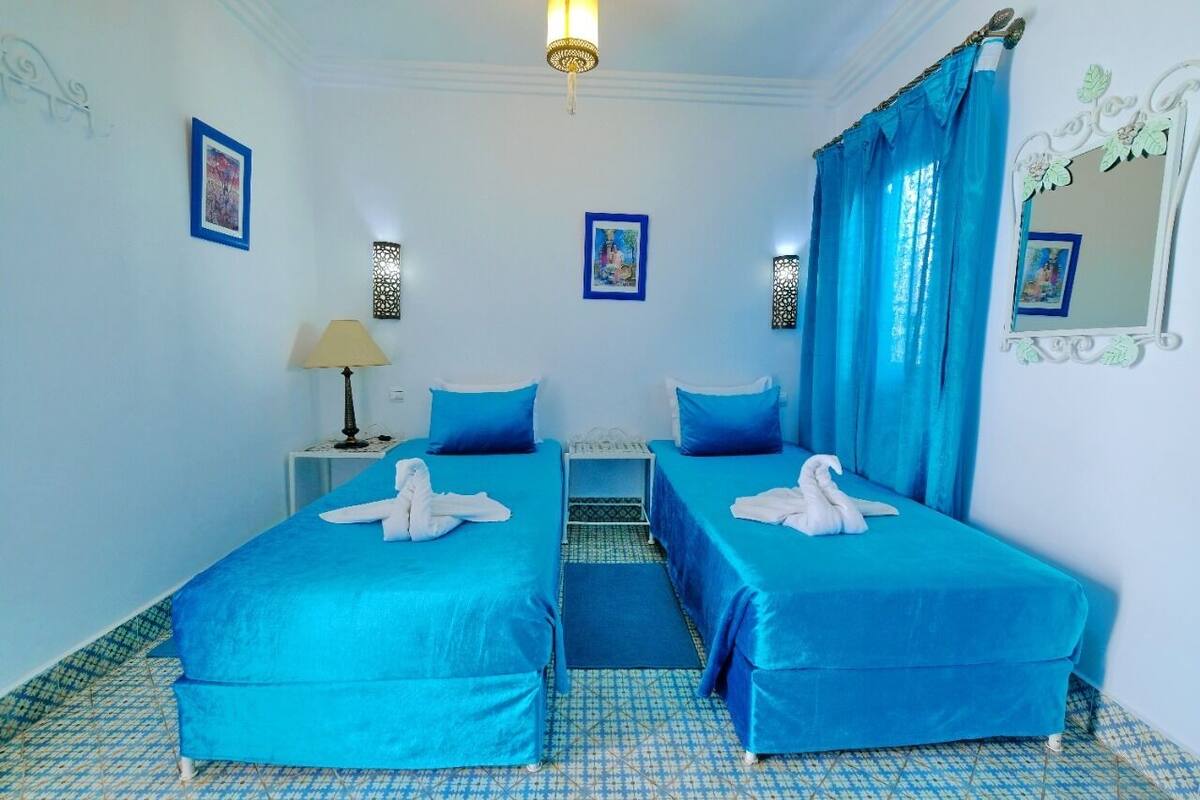 A room with two beds, a lamp, a mirror, and a patterned floor.