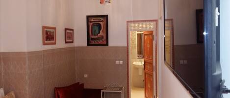 Un baño con espejo, lavamanos e inodoro. Se observan cuadros enmarcados en la pared y una lámpara decorativa colgante.