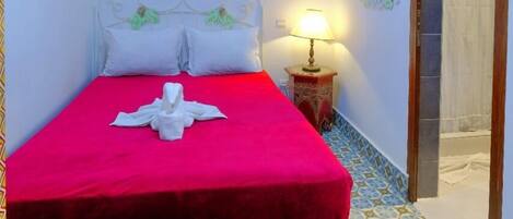 A neatly made bed with a red bedspread and white pillows, a bedside lamp, and a decorative wall piece.
