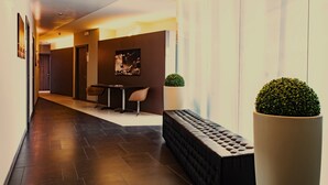 Ein moderner Hotelkorridor mit dunklem Fliesenboden, einer Sitzecke mit Sofa und Sesseln, einem kleinen Tisch und einem Blumentopf.