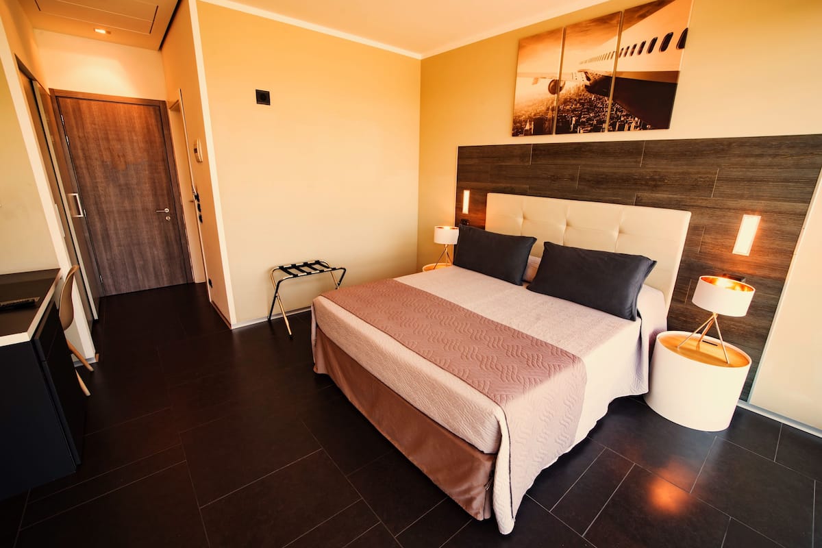 Una habitación de hotel moderna con una cama grande, una mesita de noche, una lámpara y vistas a la ciudad por la ventana.
