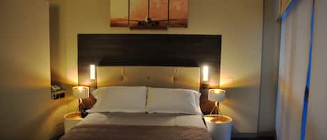 A hotel room with a large bed, two bedside tables with lamps, a cityscape artwork above the bed, and a modern headboard.