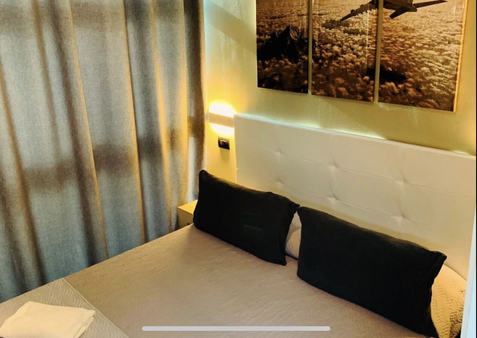 A hotel room with a large bed, two black pillows, a white headboard, and a wall-mounted light.