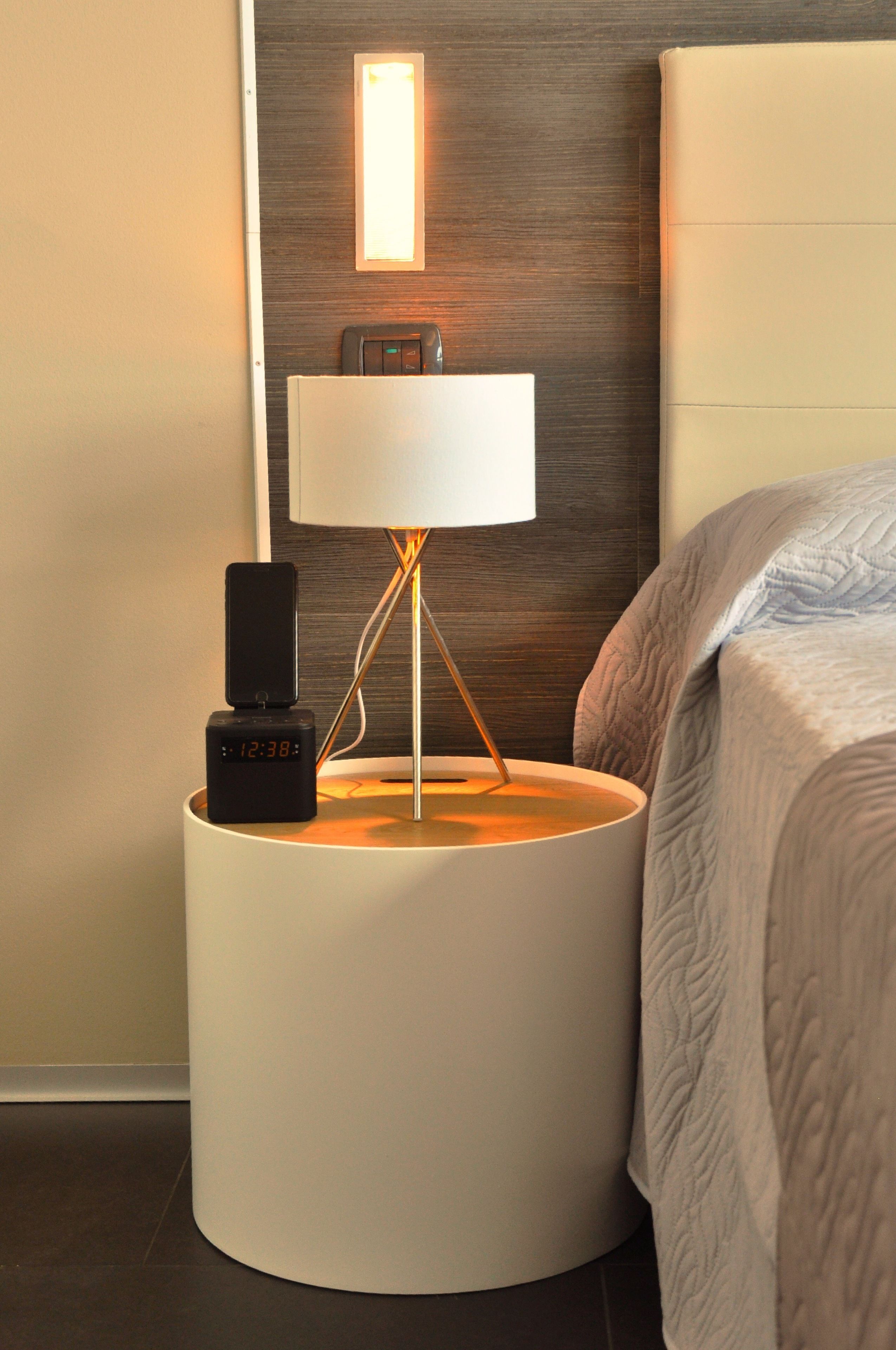 A modern bedside table with a lamp, a digital clock, and a smartphone charging dock.