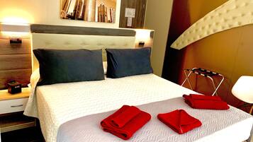 Ein Hotelzimmer mit einem Bett, zwei Kissen, einem Nachttisch, einer Lampe, einer Wanduhr und einem Handtuchhalter.