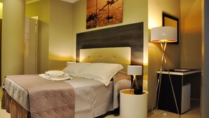 Ein Hotelzimmer mit einem großen Bett, einem Nachttisch mit Lampe, einem kleinen Schreibtisch und einem Bild an der Wand.