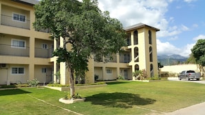 A multi-story residential building with balconies, a well-maintained lawn, and a parked vehicle.
