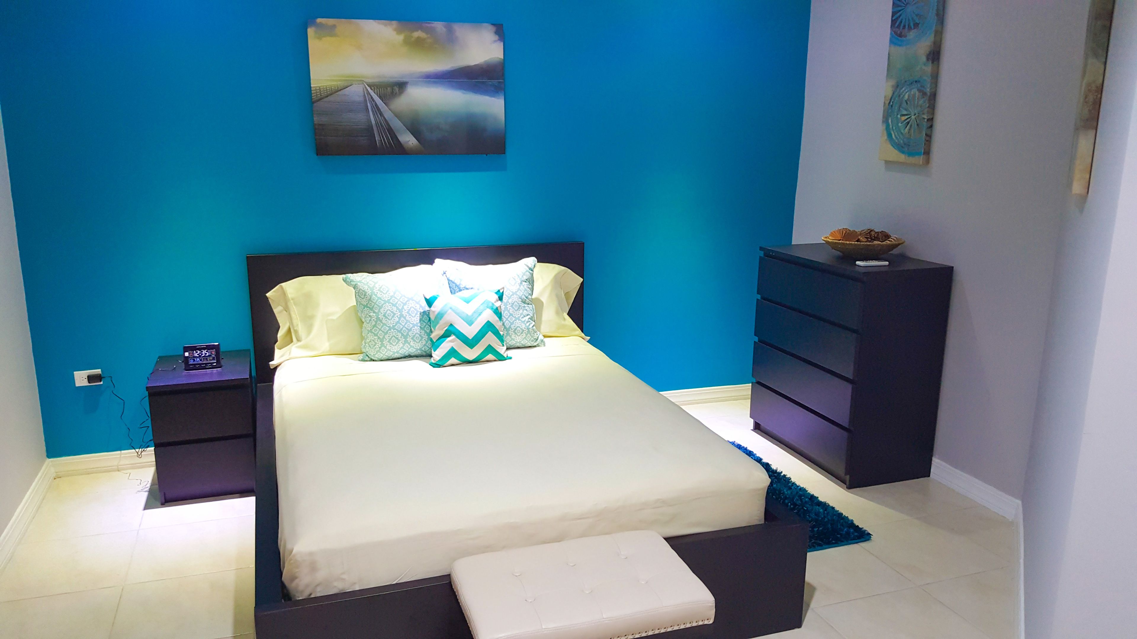Une chambre à coucher moderne, avec un lit, des tables de chevet, une commode et des œuvres d’art accrochées aux murs.