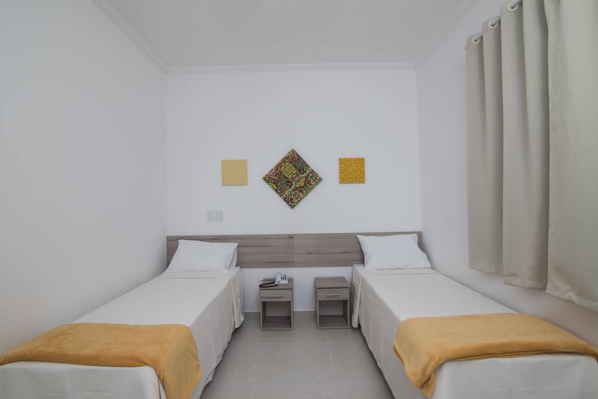 Una habitación de hotel con dos camas individuales, una mesita de noche con teléfono y un adorno en la pared.