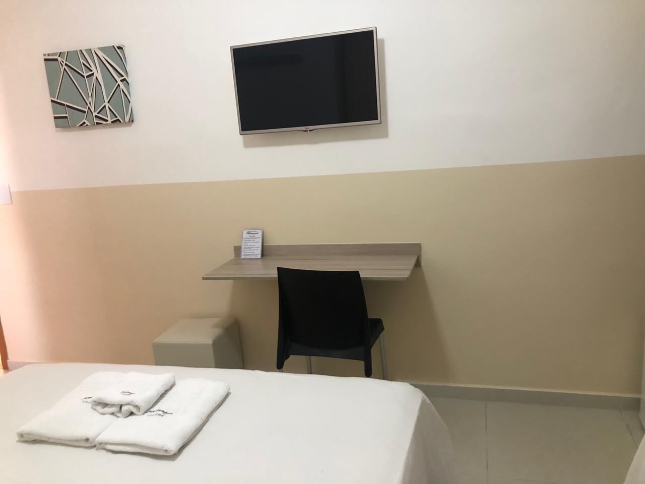 Une chambre d’hôtel équipée d’un lit, d’un bureau, d’une chaise, d’un téléviseur à écran plat et d’une œuvre d’art murale.