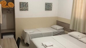 Une chambre d’hôtel avec deux lits simples, un bureau en bois, une chaise, une petite table et une armoire.