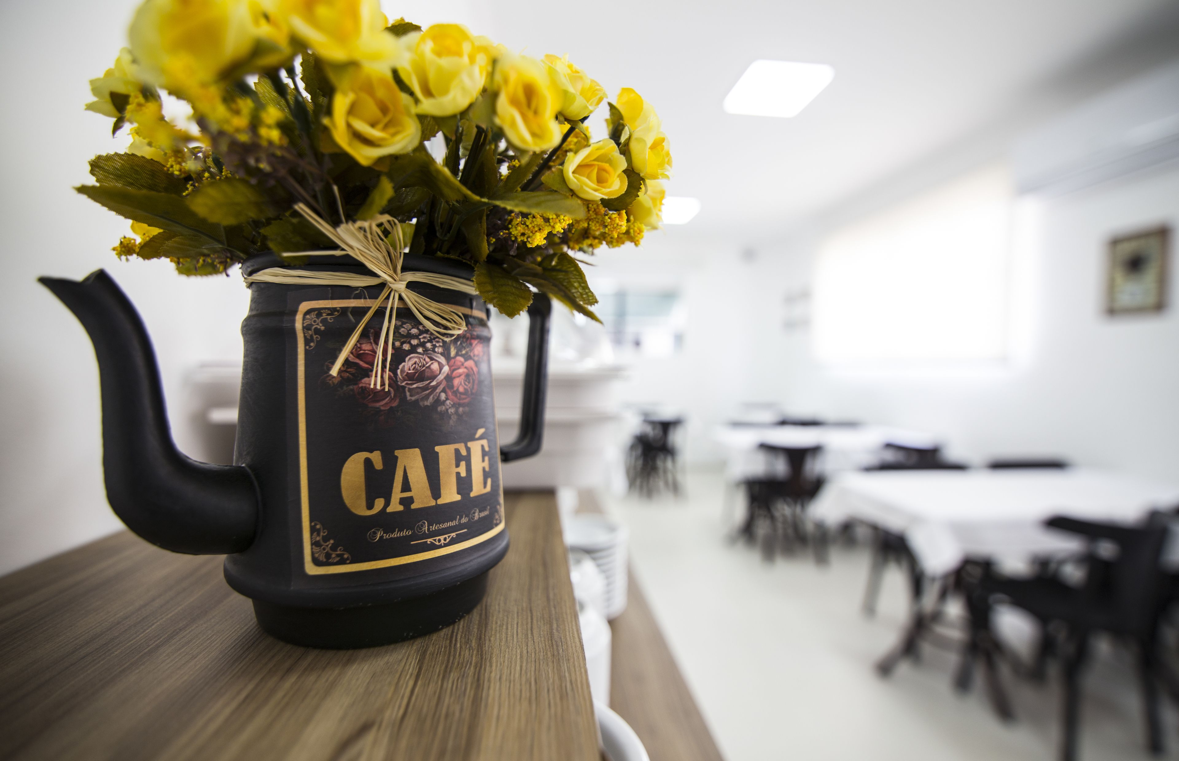 A black teapot with a label reading "CAFE" and a bouquet of yellow roses tied with a string.