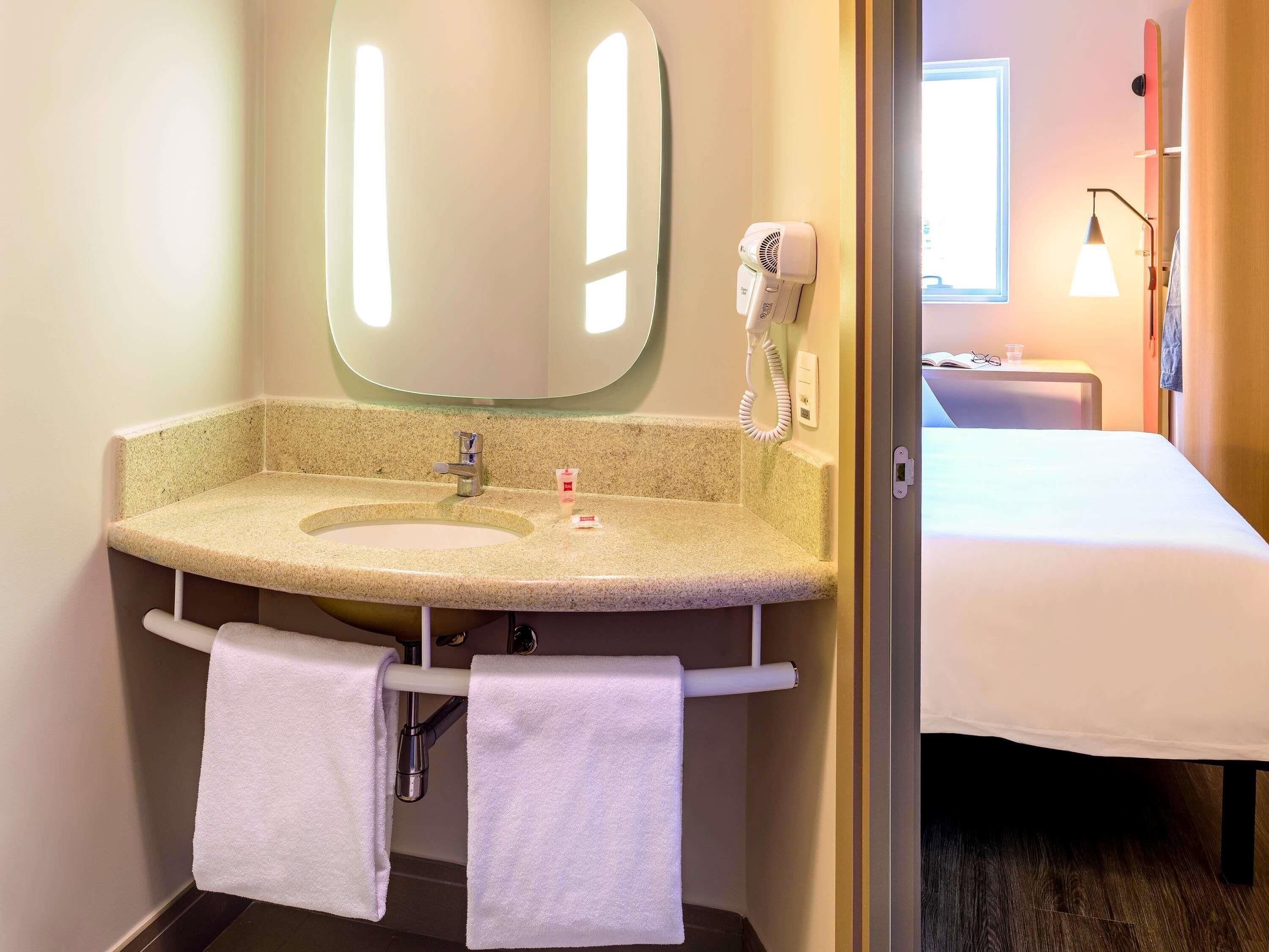 Ein Hotelbad mit Waschbecken, Spiegel, Handtuchhalter und einem Föhn.