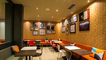 Un restaurant avec des banquettes orange, des tables blanches et des chaises noires.
