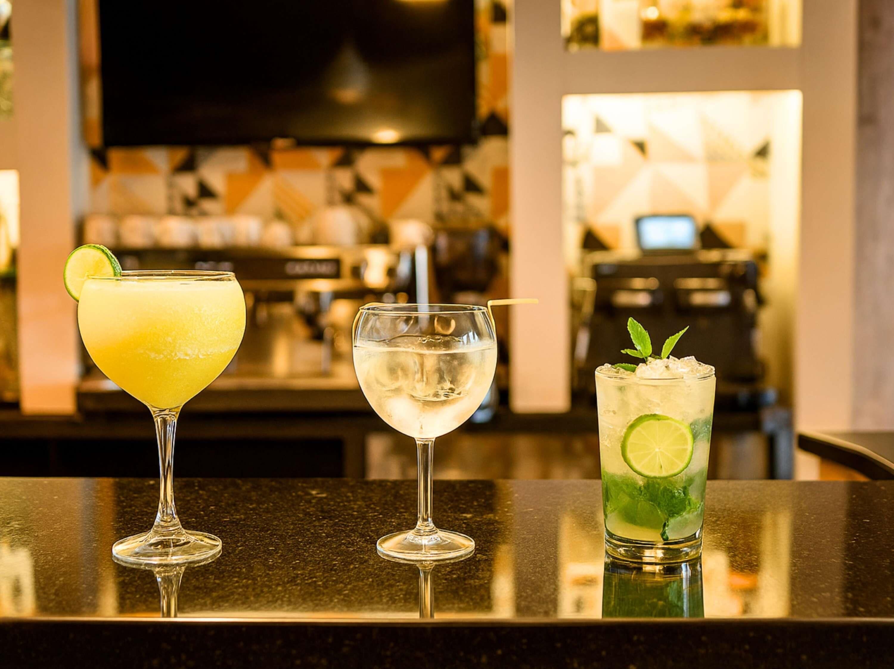 Three glasses of different beverages on a bar counter.