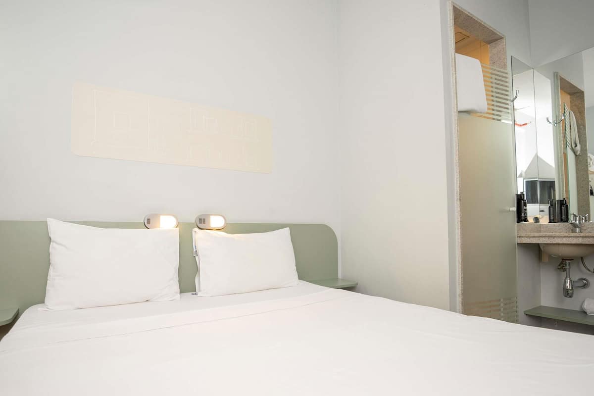 Une chambre d’hôtel avec un lit, deux lampes de chevet, un miroir et un lavabo.