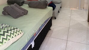 A hotel room with a bed, pillows, a TV, and a tiled floor. - Pousada Gil (Olímpia)