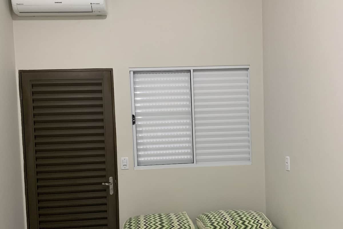 Ein Badezimmer mit einem grünen Waschbecken, einem Handtuchhalter mit gefalteten Handtüchern, einem Fenster mit Jalousien und einer wandmontierten Klimaanlage.