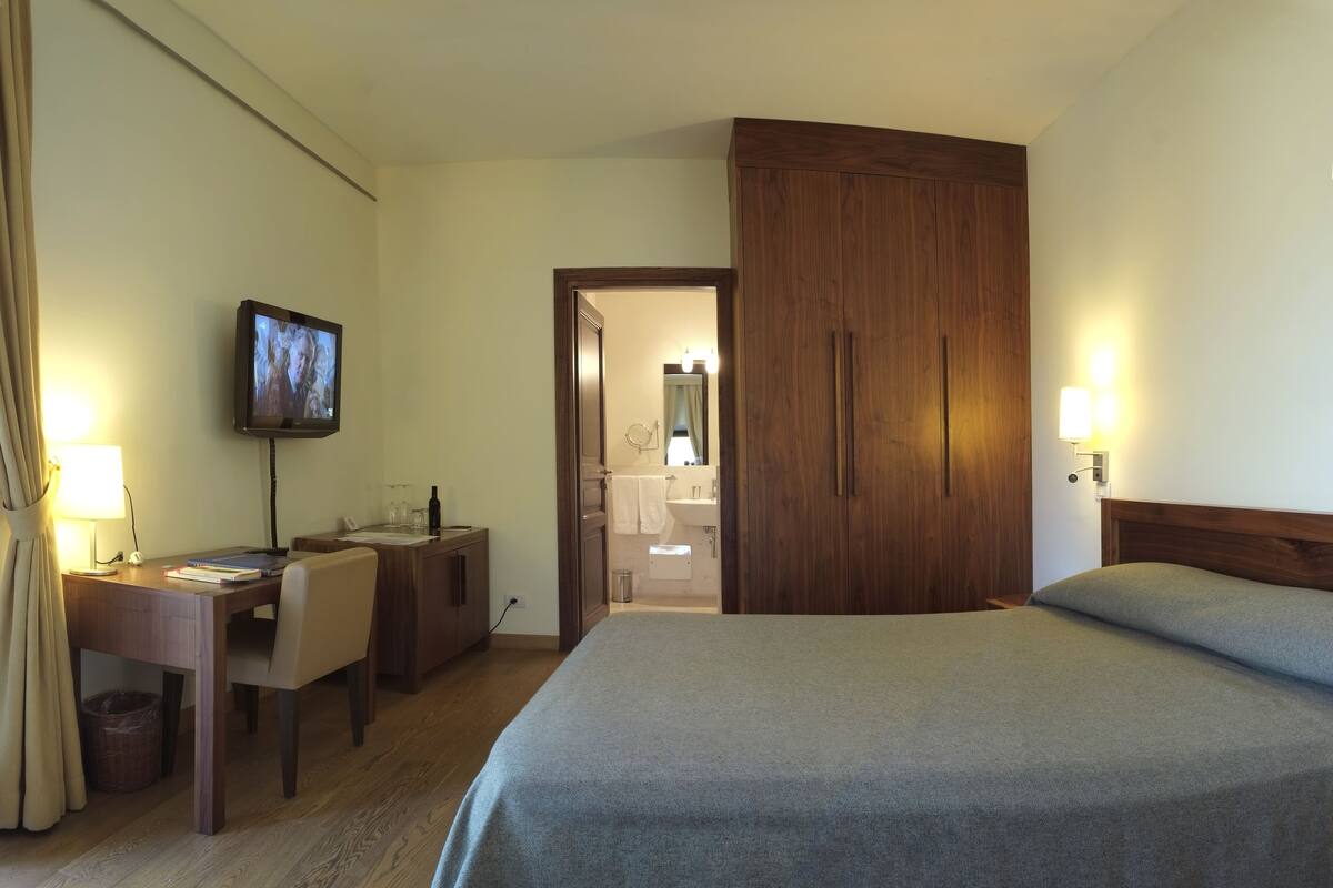 A hotel room with a bed, a desk with a chair, a TV, and a wardrobe.
