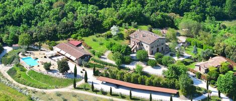 An aerial view of a property with a swimming pool, a large building with a red roof, and a long covered walkway.
