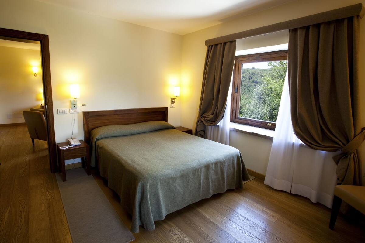 A hotel room with a bed, bedside table, lamp, and a window with curtains.