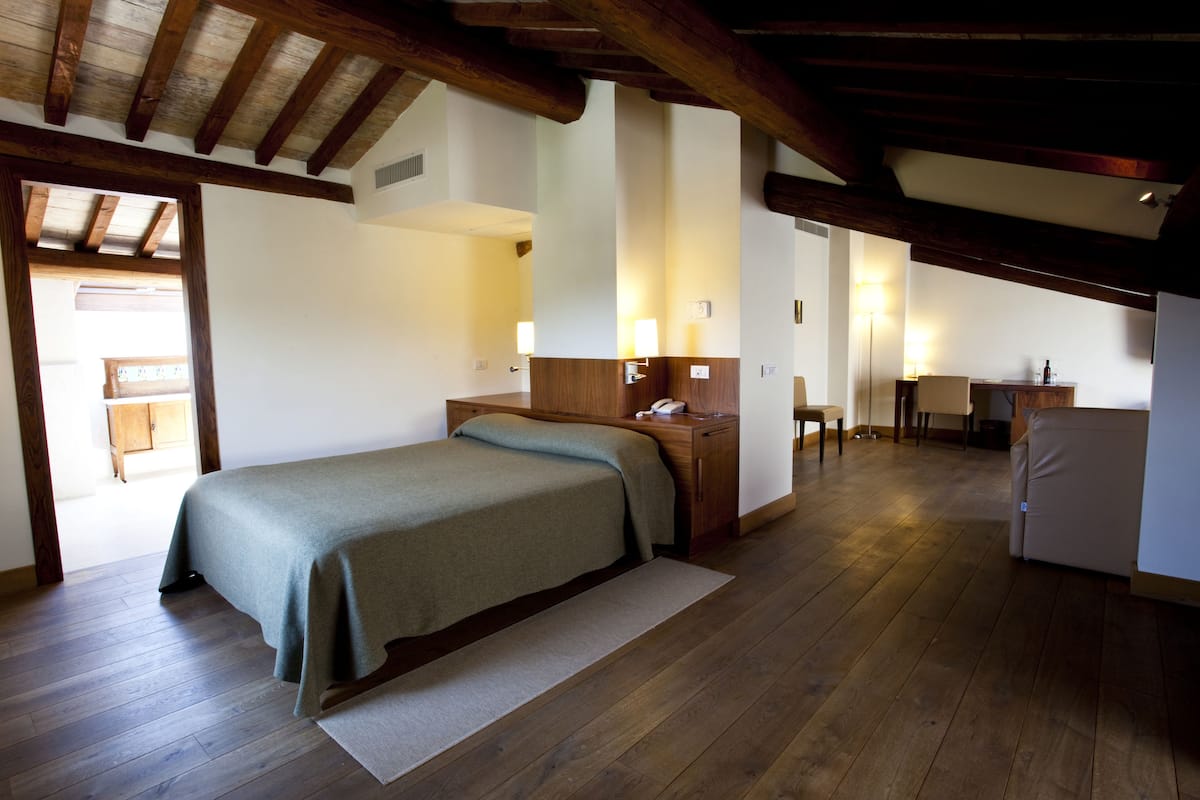 A bedroom with a bed, wooden floor, and a desk with a chair.
