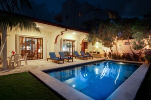 A swimming pool with lounge chairs, a dining area with chairs, and a well-lit patio with plants. - Casa Anita (Puerto Morelos)