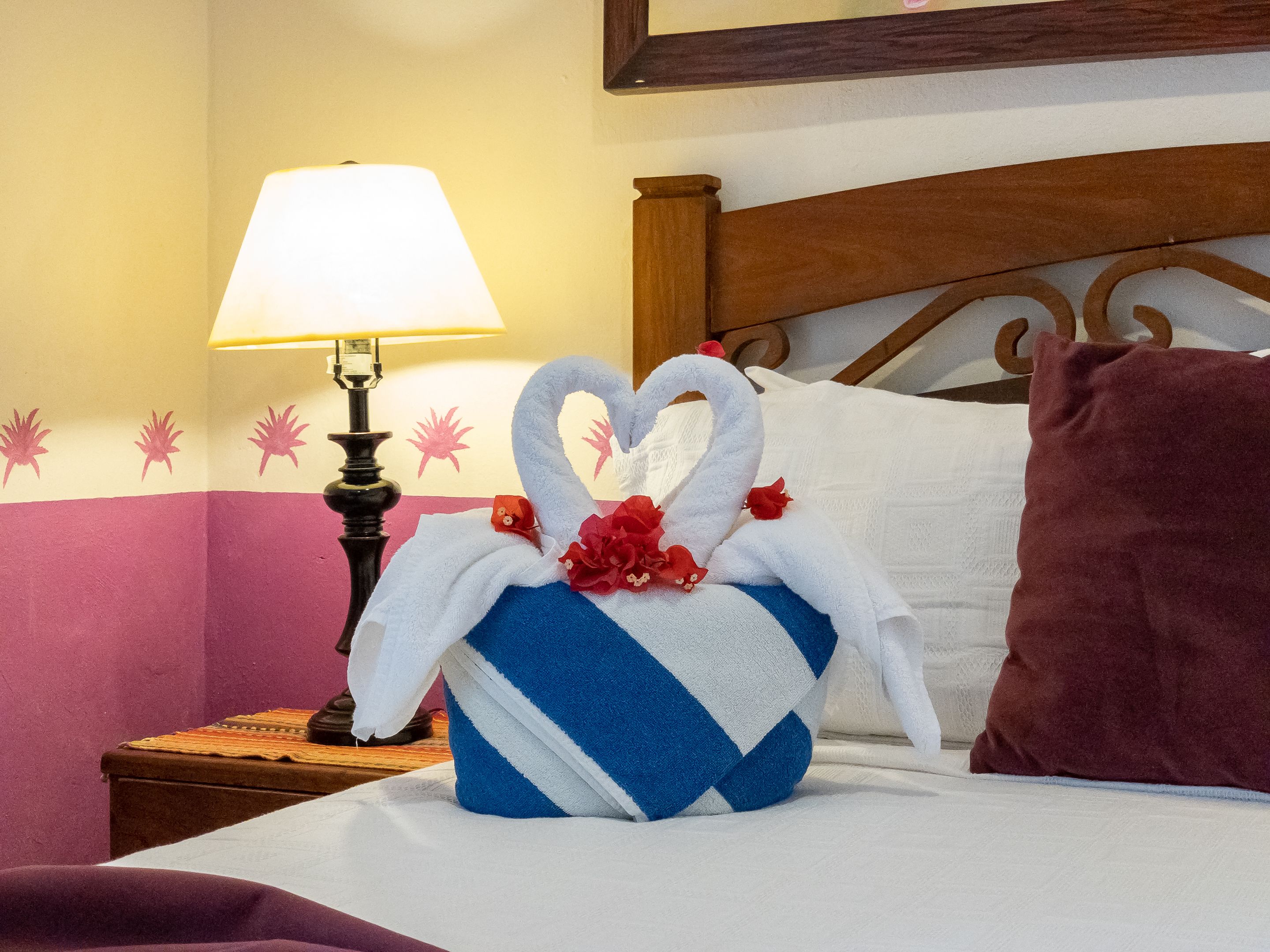 A neatly made bed with a decorative towel shaped like a swan, a lamp, and a wooden headboard.