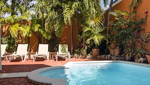 Une piscine bordée de briques, entourée de palmiers et de chaises longues.