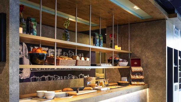A modern breakfast bar with shelves of bread, pastries, and condiments. - ibis budget Rotterdam The Hague Airport (Rotterdam)