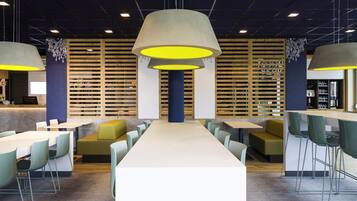 Un restaurant moderne avec des tables hautes, des chaises vertes et des luminaires suspendus.