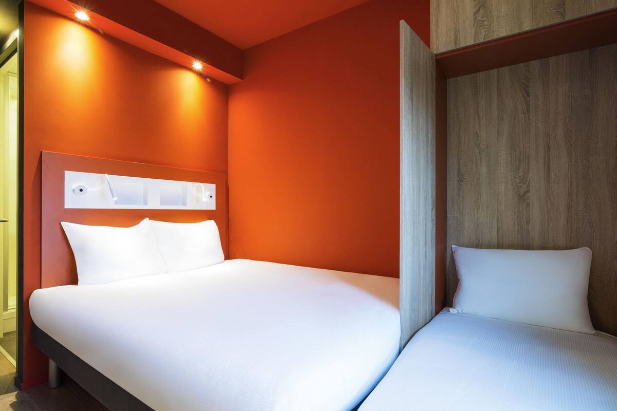 Una habitación de hotel con cama doble, cabecero de madera y una lámpara fijada a la pared.