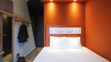 Une chambre d’hôtel moderne avec un grand lit, un plancher en bois, un porte-manteau et un miroir.
