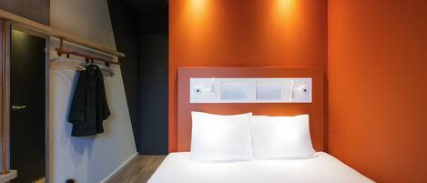 A modern hotel room with a large bed, a wooden floor, a coat rack, and a mirror.