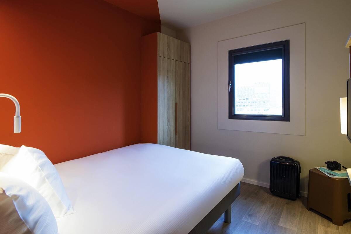Een hotelkamer met een bed, een raam met uitzicht, een koffer en een lamp.