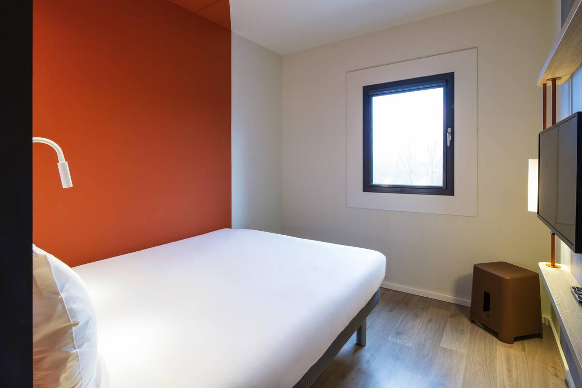 Una habitación pequeña y moderna con una cama individual, una ventana, un televisor y un altavoz.