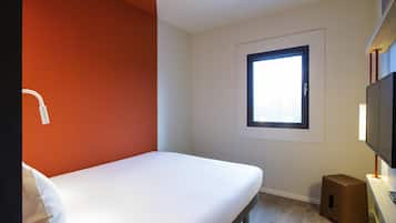 Una habitación pequeña y moderna con una cama individual, una ventana, un televisor y un altavoz.