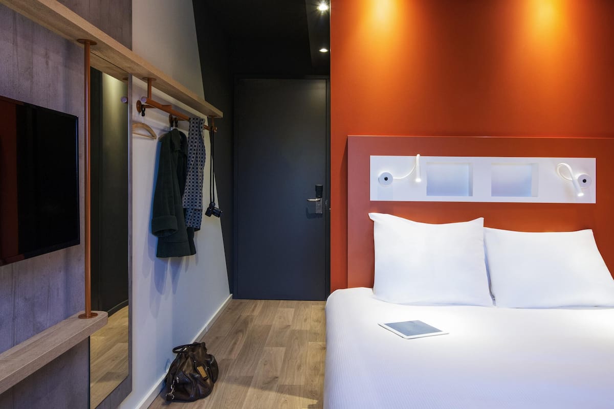 Een moderne hotelkamer met een bed, een televisie, een kapstok en een deur.