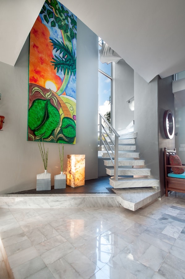 Um interior moderno com uma escadaria de mármore, uma pintura abstrata colorida e dois vasos com plantas.