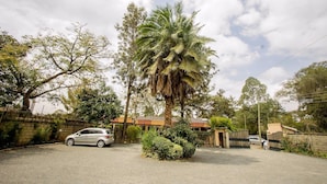 A residential area with a parked car, a palm tree, and a gated entrance. - Konar House Kilimani (Nairobi)