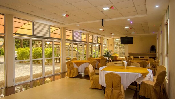 A spacious indoor dining area with large windows, tables covered with yellow tablecloths, and chairs with yellow covers. - Konar House Kilimani (Nairobi)