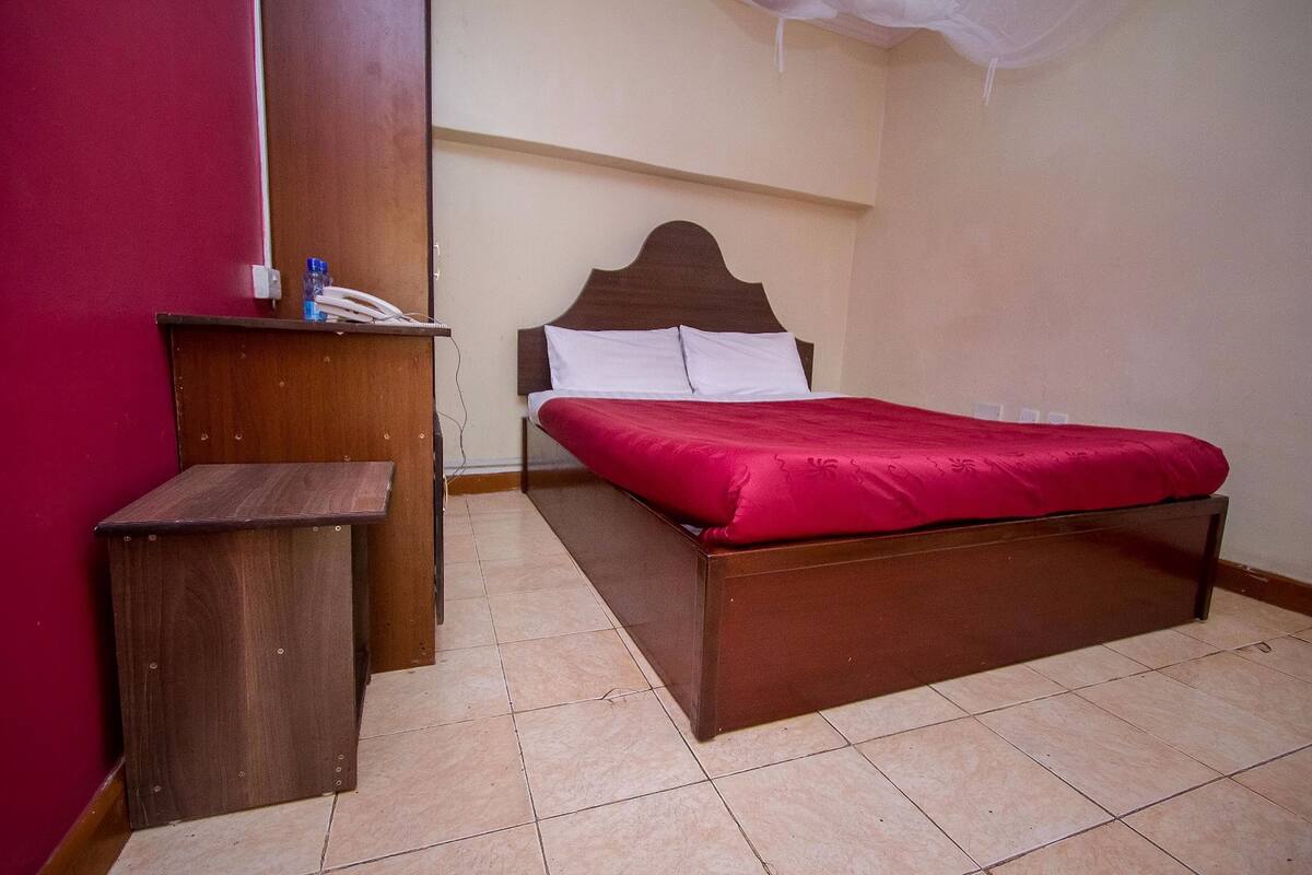 A bedroom with a wooden bed, a bedside table, and a red wall.