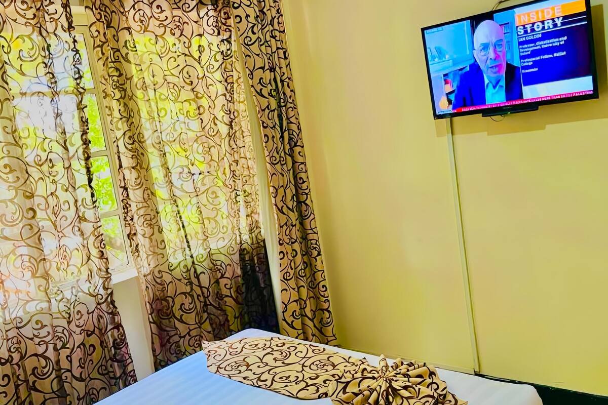A hotel room with a bed, a TV on the wall, and curtains with a floral pattern.