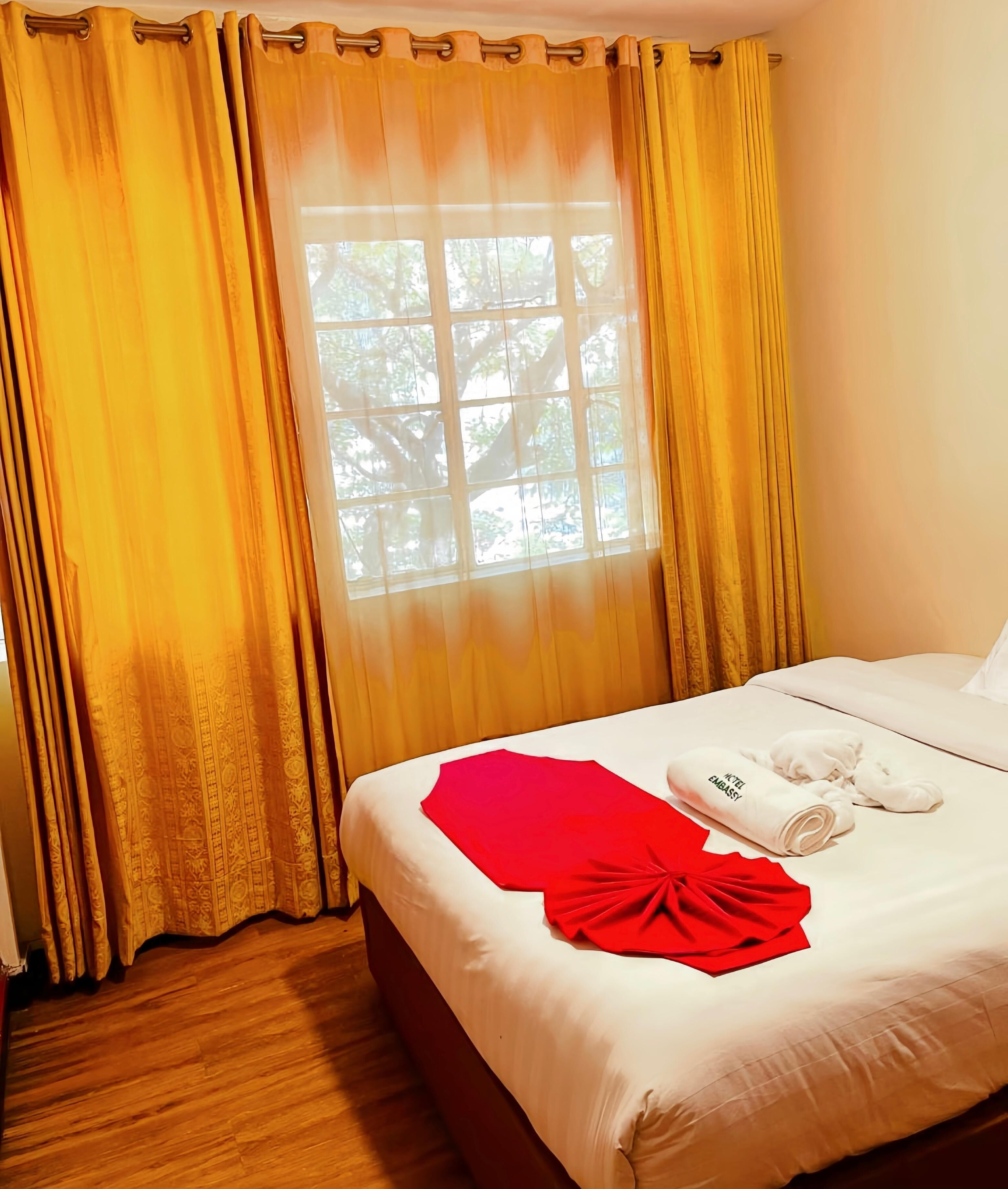 A hotel room with a bed, a window with curtains, and a view of trees outside.