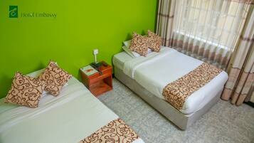 Habitación de hotel con dos camas, paredes verdes, una mesita de noche de madera con un teléfono y una ventana con cortinas.